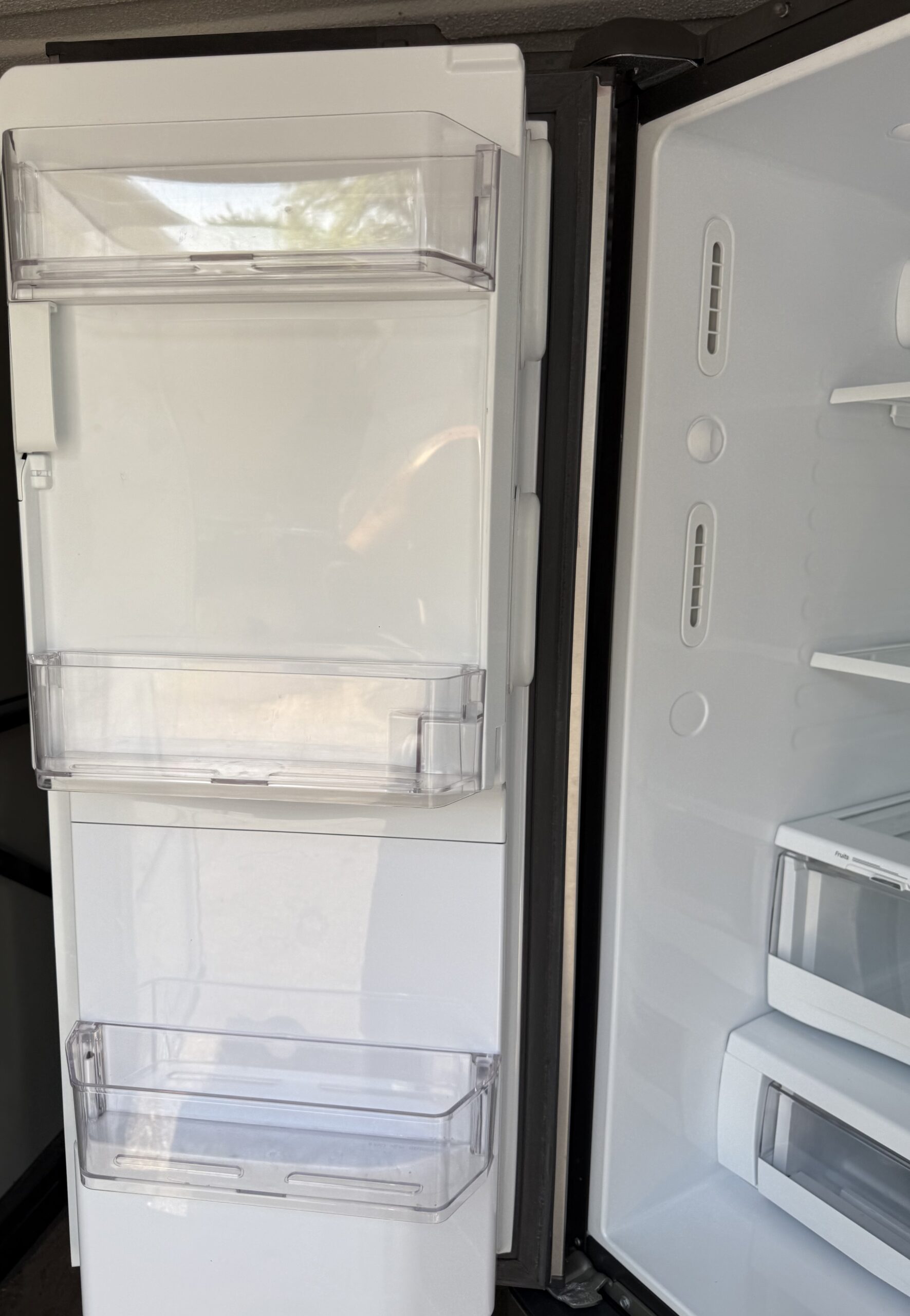 GE refrigerator left door interior showing water/ice dispenser back panel and door bin storage