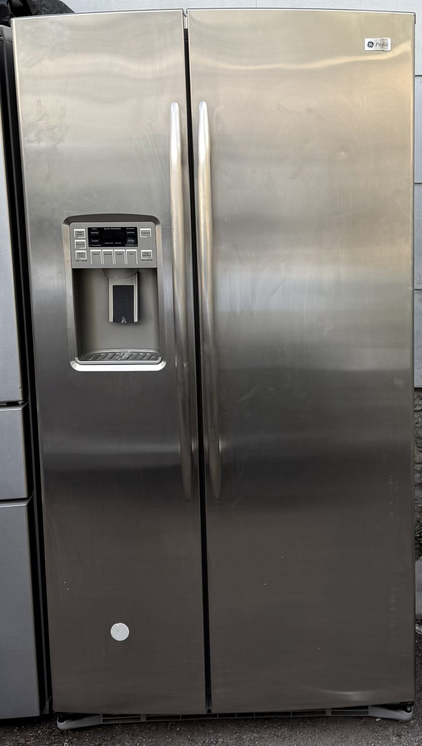 GE Profile side-by-side refrigerator stainless steel — front view with ice and water dispenser.