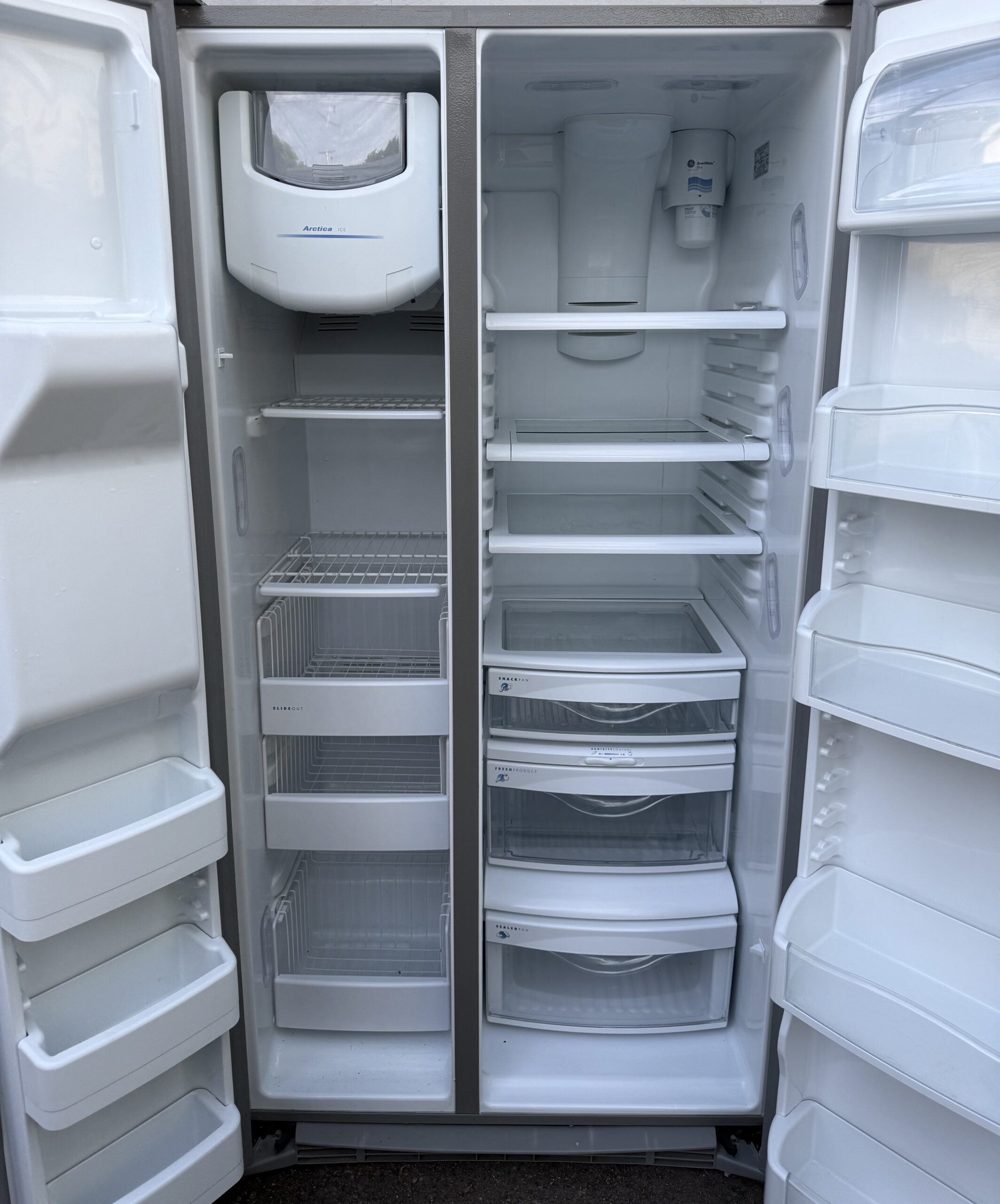 GE Profile side-by-side refrigerator — interior shelving and freezer compartment with both doors open.