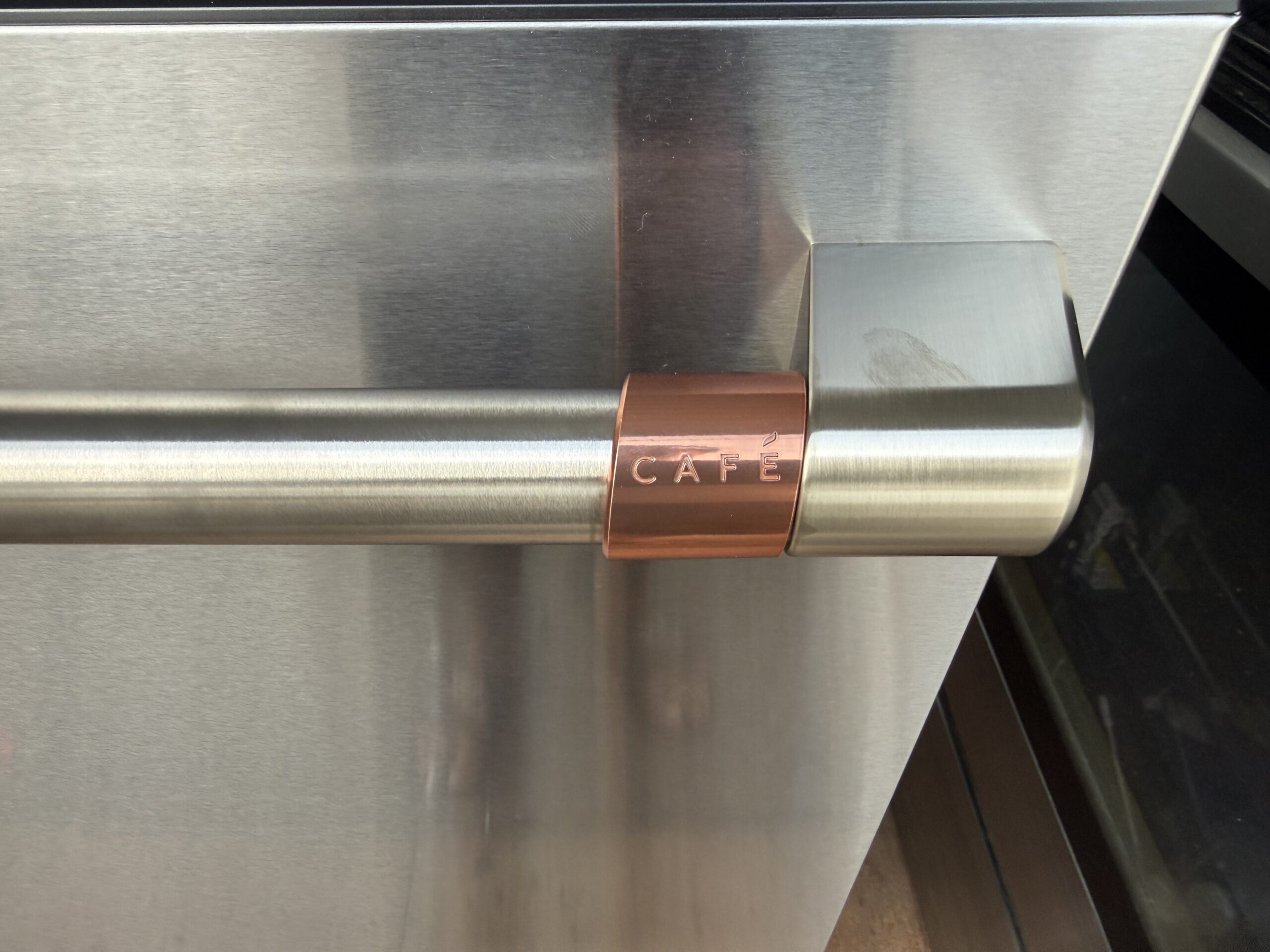 Close-up of the Café dishwasher brushed stainless handle with the signature copper accent collar