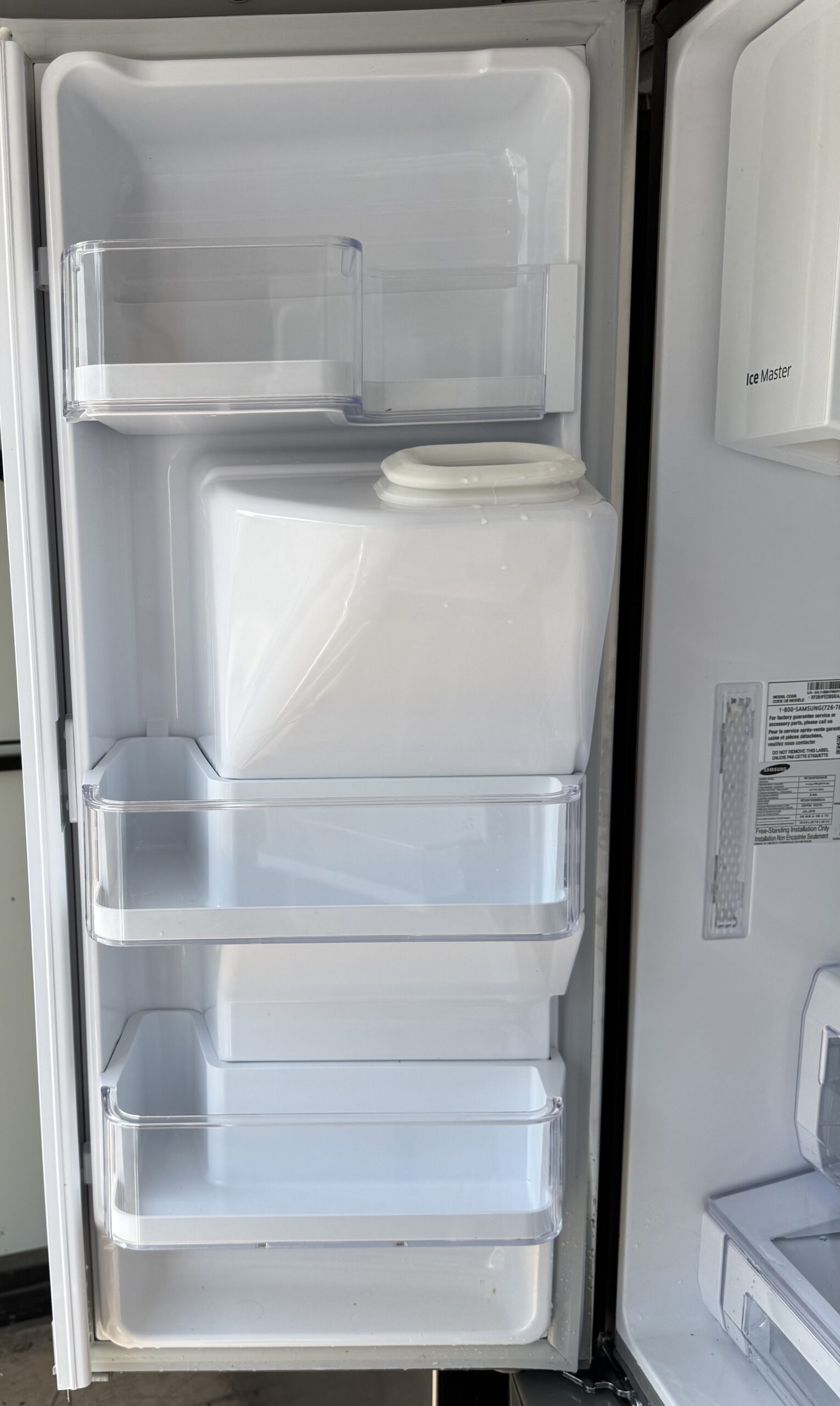 Samsung French door refrigerator left door open showing Ice Master ice maker and door bins