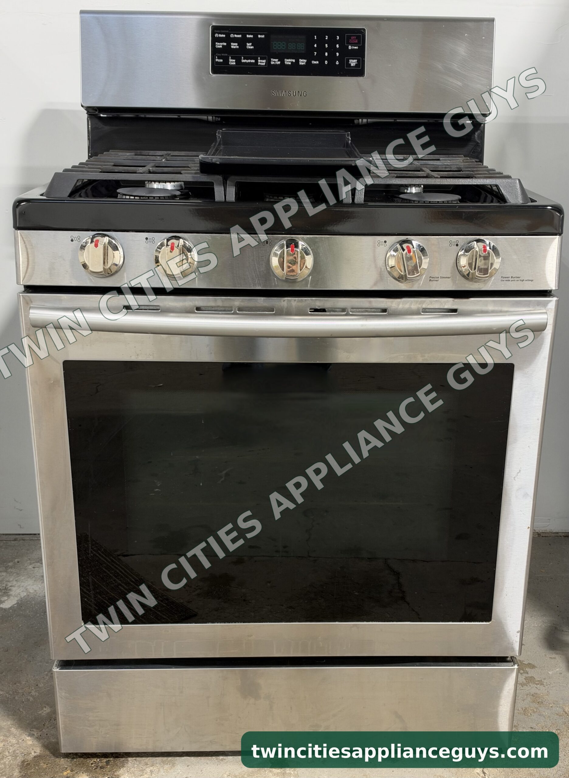 Stainless Samsung gas range front view with five burner knobs and the oven door closed
